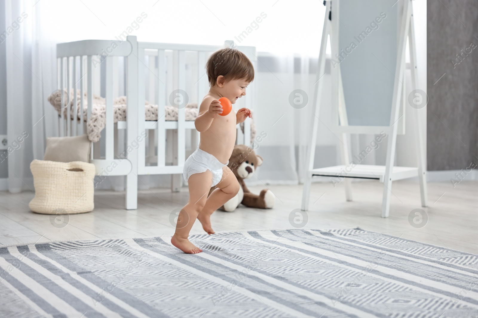 Photo of Cute little child in diaper with toy at home