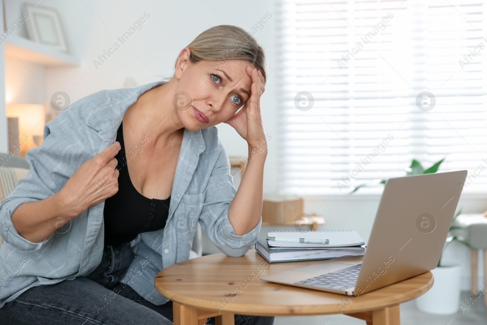 Photo of Menopause. Woman suffering from hot flash at table with laptop indoors