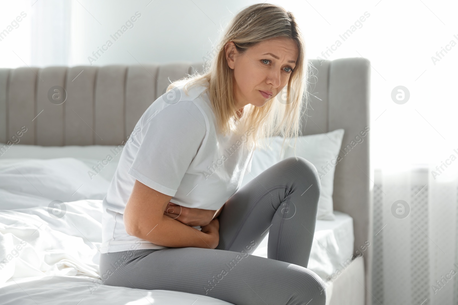 Photo of Menopause. Woman suffering from abdominal pain on bed at home