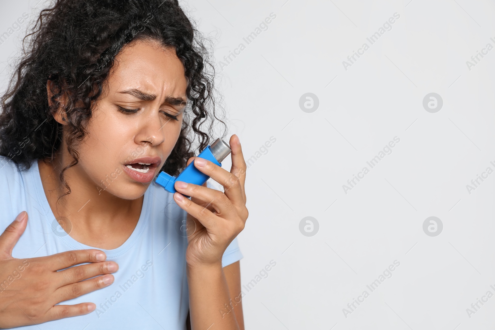 Photo of Young woman using asthma inhaler on white background. Space for text