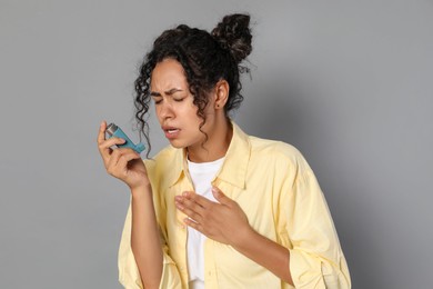 Young woman using asthma inhaler on grey background