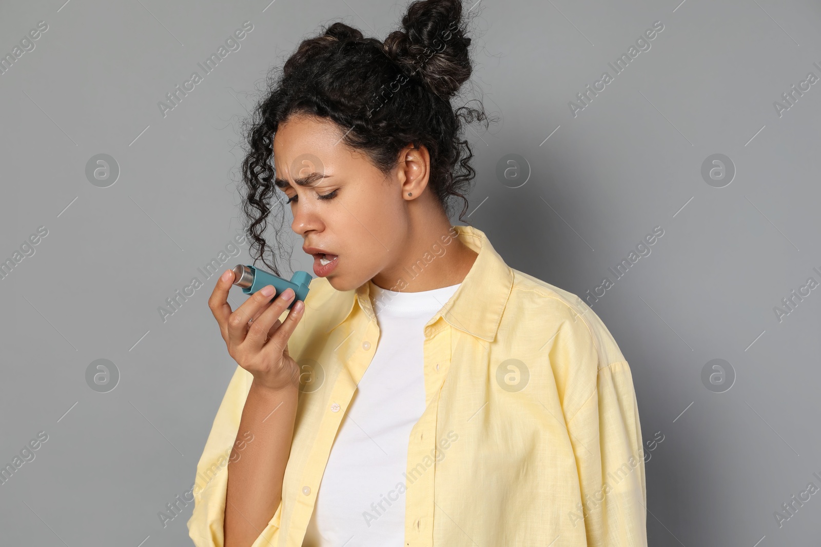 Photo of Young woman using asthma inhaler on grey background