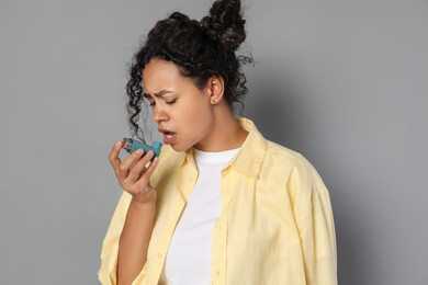 Young woman using asthma inhaler on grey background