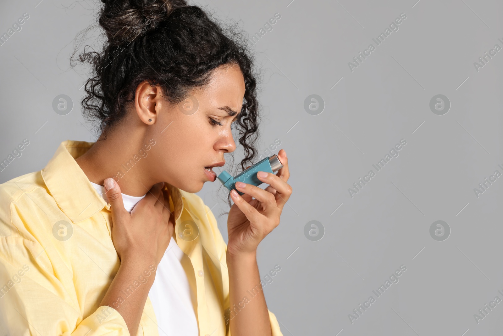 Photo of Young woman using asthma inhaler on grey background. Space for text