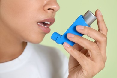 Photo of Young woman using asthma inhaler on light green background, closeup