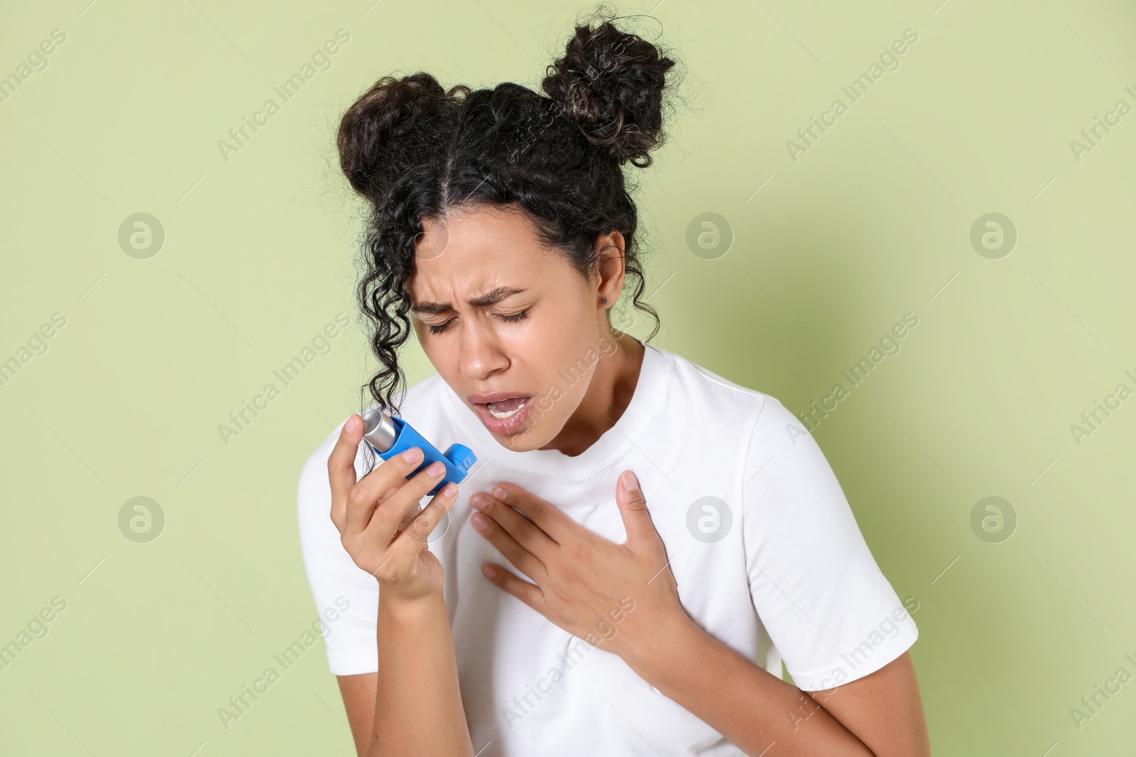 Photo of Young woman using asthma inhaler on light green background