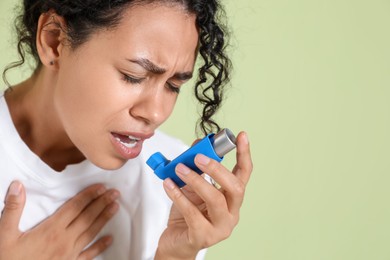 Photo of Young woman using asthma inhaler on light green background, closeup. Space for text