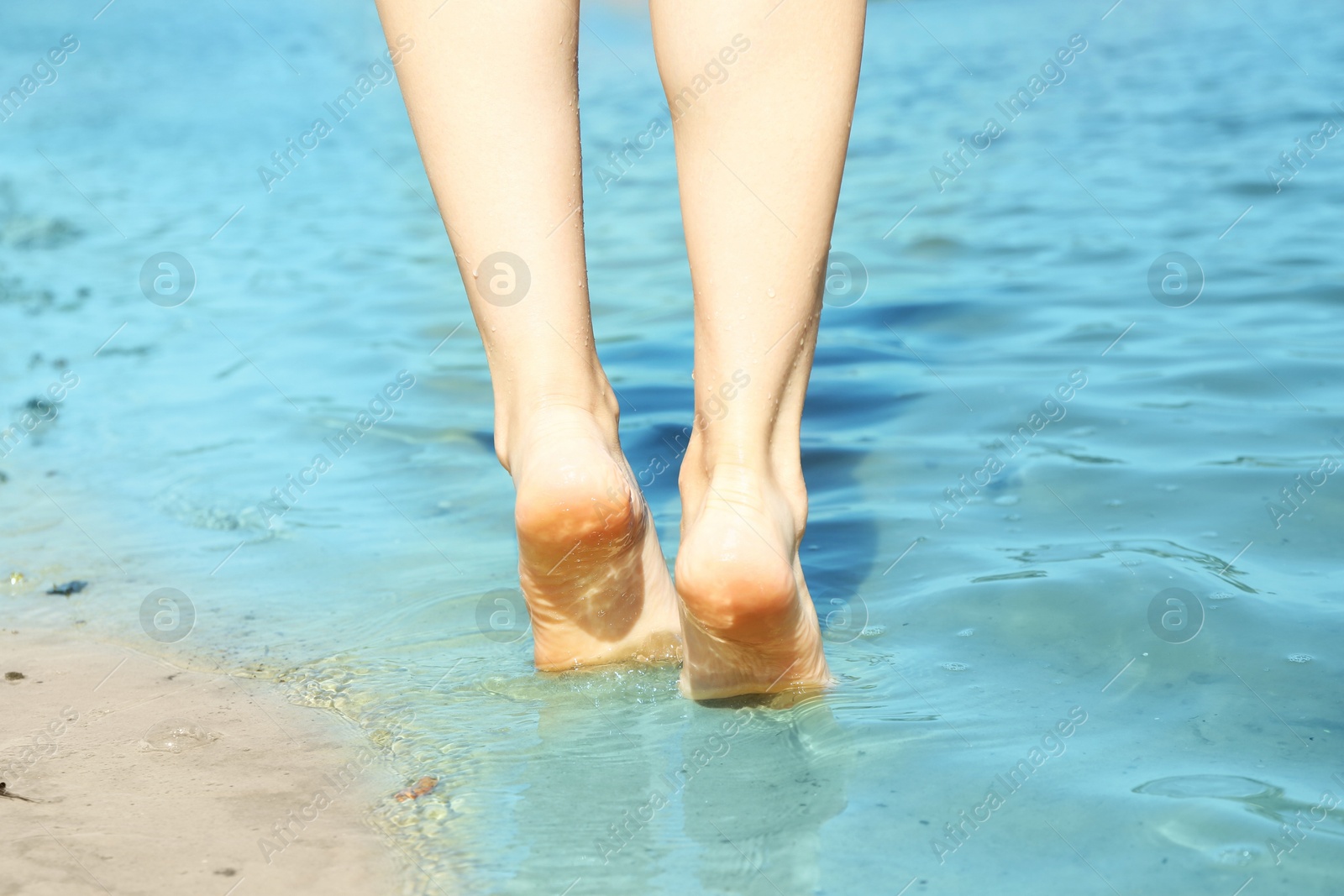 Photo of Woman walking barefoot through water on riverbank, closeup