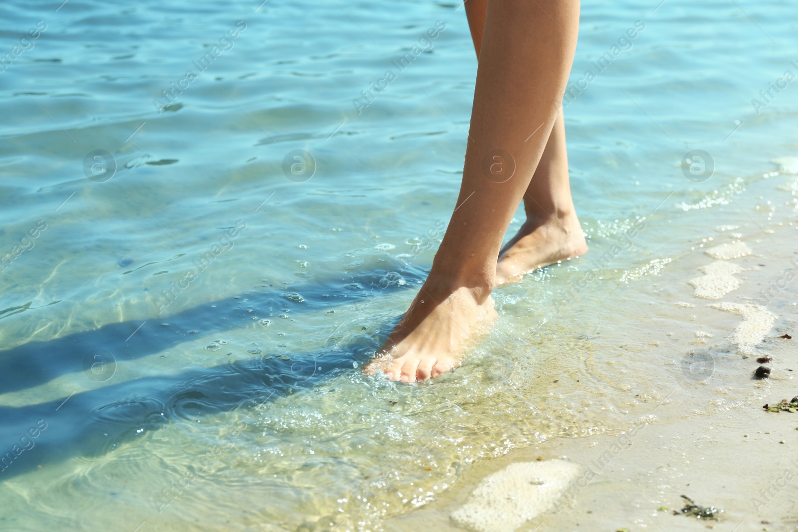 Photo of Woman walking barefoot through water on riverbank, closeup