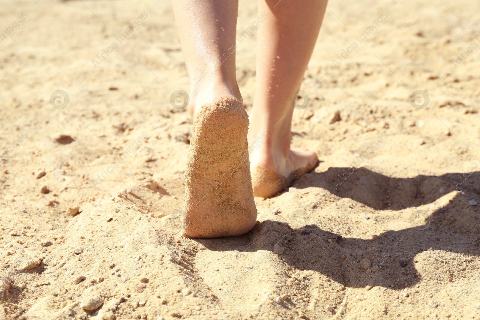 Photo of Woman walking barefoot on sand outdoors, closeup