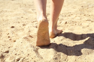 Photo of Woman walking barefoot on sand outdoors, closeup