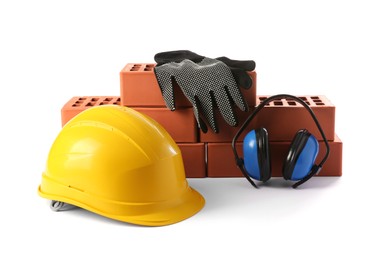 Photo of Yellow hard hat, red bricks, gloves and earmuffs isolated on white. Building material and safety equipment