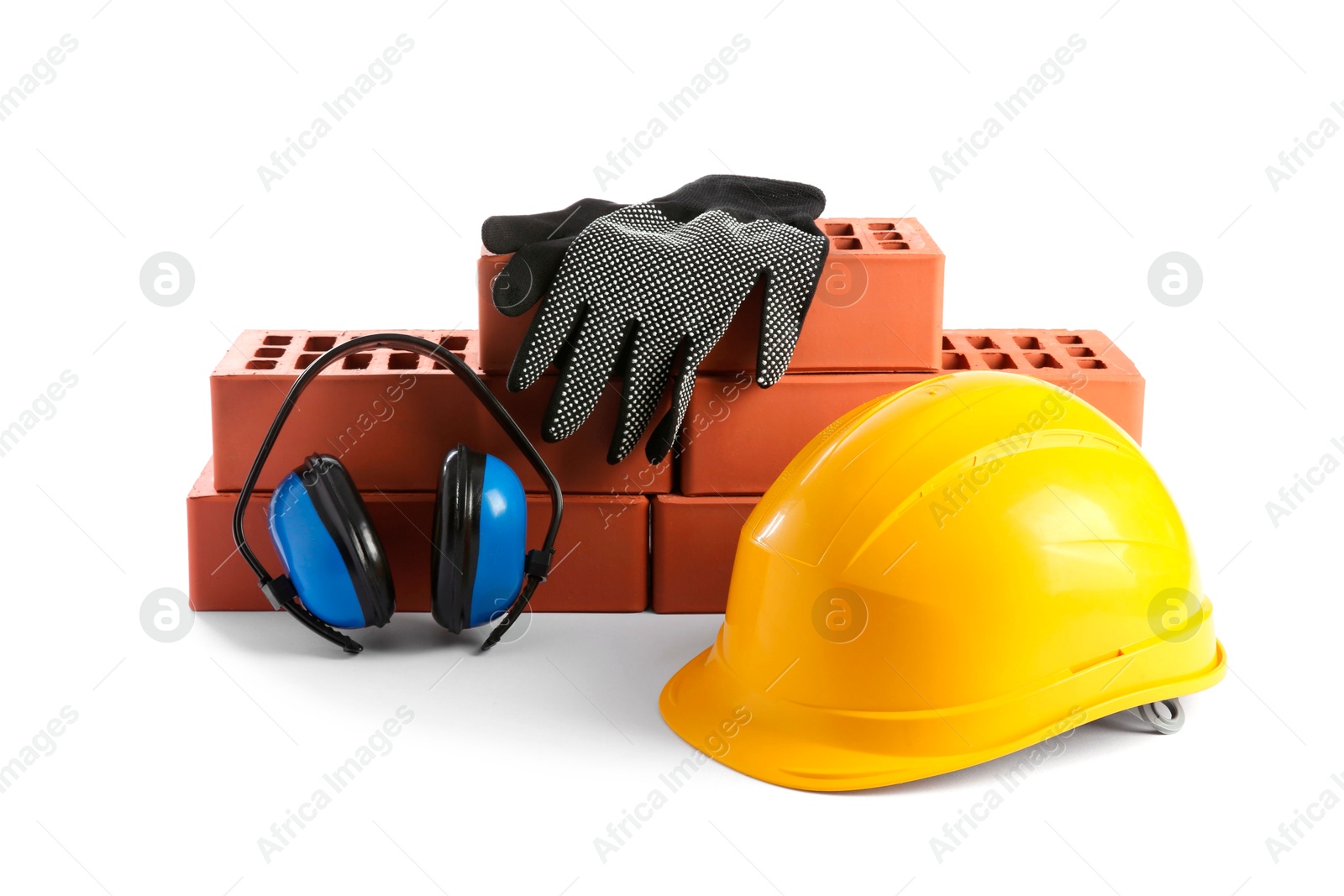 Photo of Yellow hard hat, red bricks, gloves and earmuffs isolated on white. Building material and safety equipment