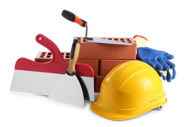 Photo of Yellow hard hat, red bricks, gloves, trowel and putty knives isolated on white. Building material and construction tools