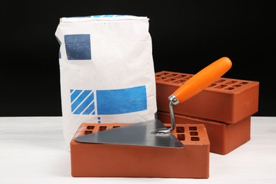 Cement powder in bag, trowel and red bricks on white wooden table. Building materials and construction tools