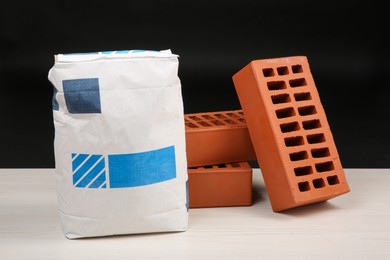 Red bricks and bag of cement on light wooden table against black background. Building materials