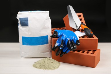 Red bricks, cement powder, putty knife and gloves on light wooden table against black background. Building materials