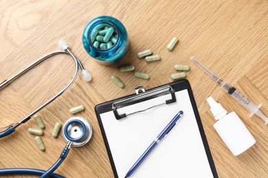 Photo of Pharmacist. Many pills, stethoscope, syringe, clipboard and bottle of medical drops on wooden table, flat lay