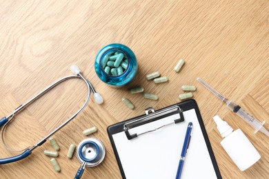 Photo of Pharmacist. Many pills, stethoscope, syringe, clipboard and bottle of medical drops on wooden table, flat lay