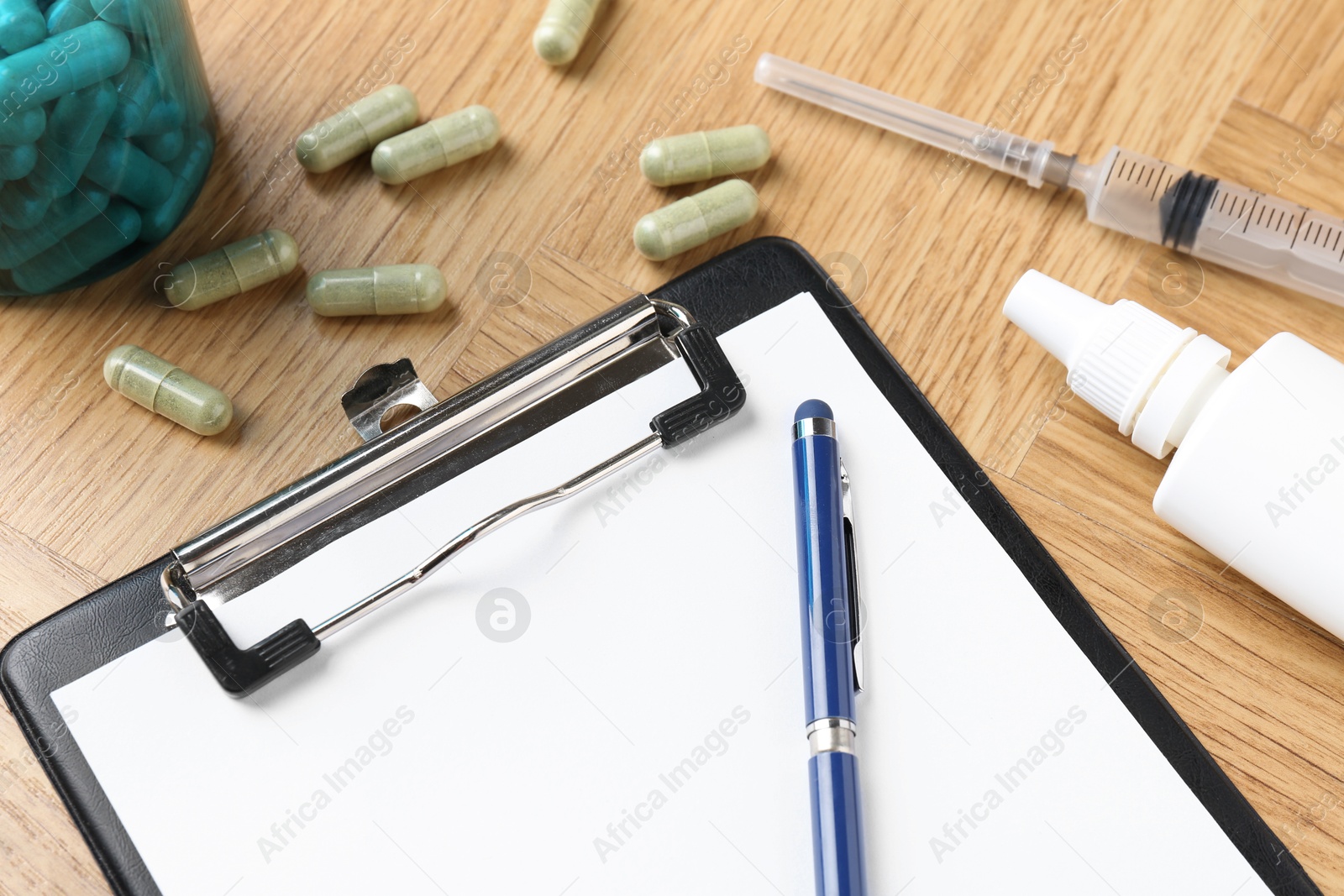 Photo of Pharmacist. Many pills, stethoscope, syringe, clipboard and bottle of medical drops on wooden table, closeup