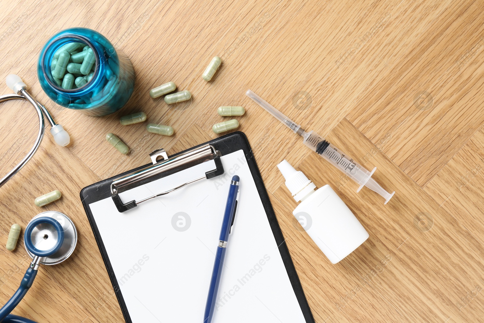 Photo of Pharmacist. Many pills, stethoscope, syringe, clipboard and bottle of medical drops on wooden table, flat lay