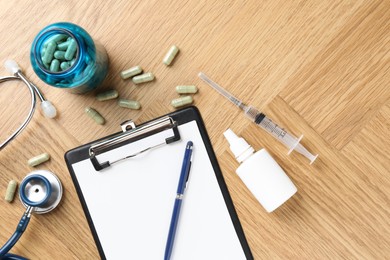 Pharmacist. Many pills, stethoscope, syringe, clipboard and bottle of medical drops on wooden table, flat lay