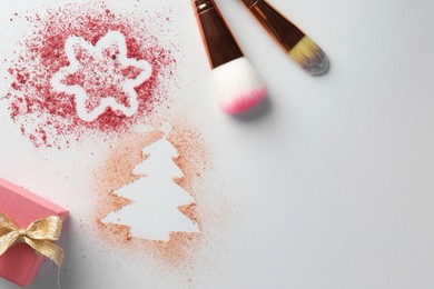 Christmas decorations made of powder and blush, gift box and makeup brushes on white background, flat lay. Space for text