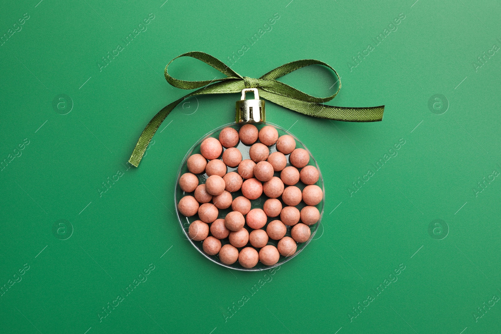 Photo of Christmas ball made of cosmetic product and bow on green background, top view