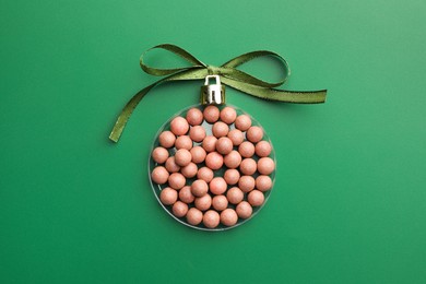 Christmas ball made of cosmetic product and bow on green background, top view