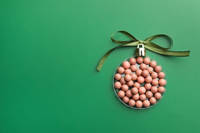 Christmas ball made of cosmetic product and bow on green background, top view. Space for text