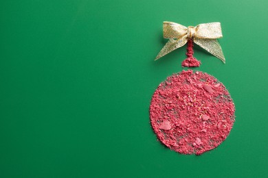 Photo of Christmas ball made of blush and bow on green background, top view. Space for text