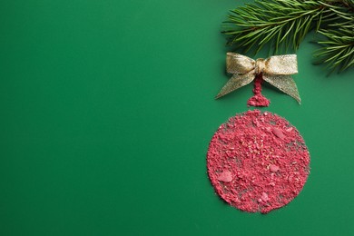 Photo of Christmas ball made of blush with bow and fir branch on green background, top view. Space for text