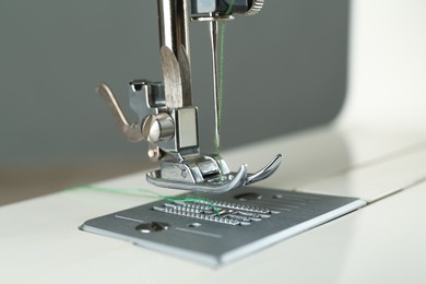 Photo of Sewing machine with green thread on grey background, closeup