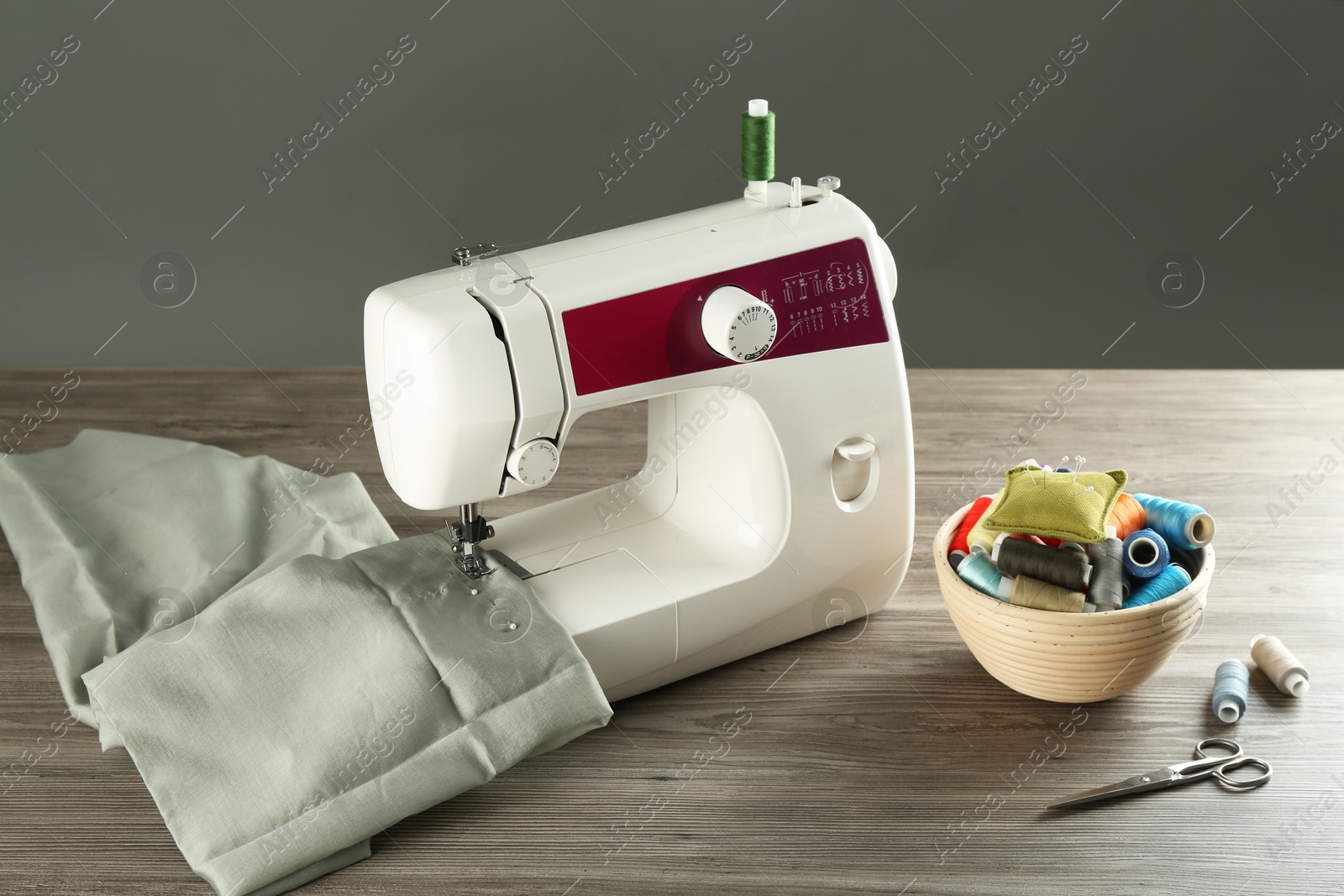 Photo of Sewing machine with fabric and tools on wooden table against grey background