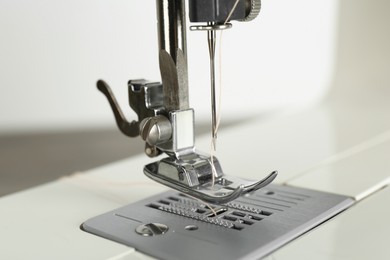 Photo of Sewing machine with beige thread on light background, closeup