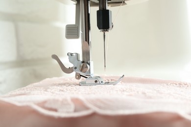 Photo of Sewing fabric with machine indoors, closeup view