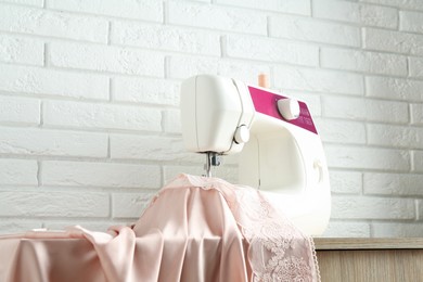 Photo of Sewing machine with fabric on wooden table indoors