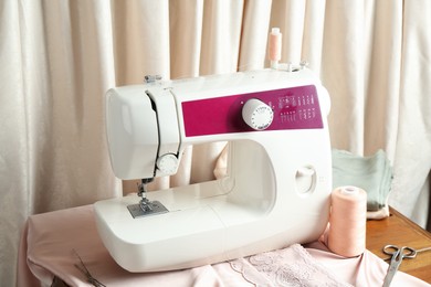 Photo of Sewing machine with fabric and tools on table indoors