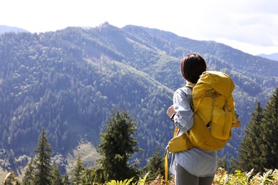 Photo of Young hiker with backpack in mountains on sunny day, back view