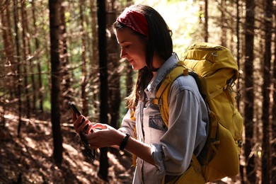 Photo of Young hiker with backpack using smartphone in forest