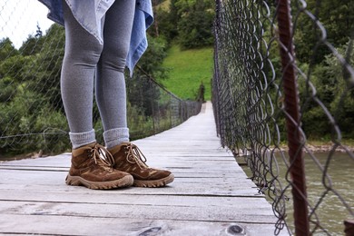 Photo of Young hiker wearing trekking shoes on wooden bridge over river, closeup