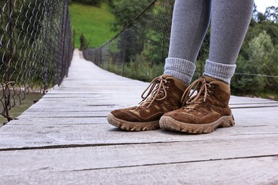 Photo of Young hiker wearing trekking shoes on wooden bridge over river, closeup