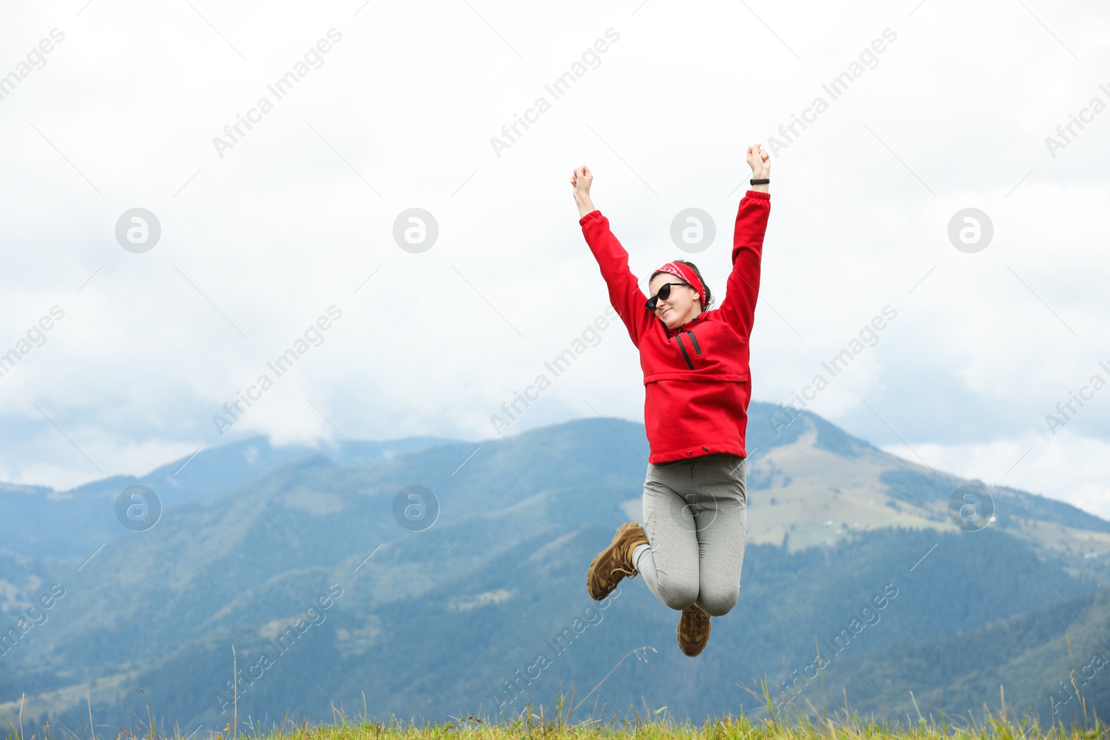 Photo of Happy young hiker jumping in mountains, low angle view. Space for text