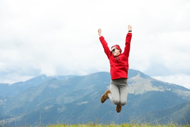 Photo of Happy young hiker jumping in mountains, low angle view. Space for text