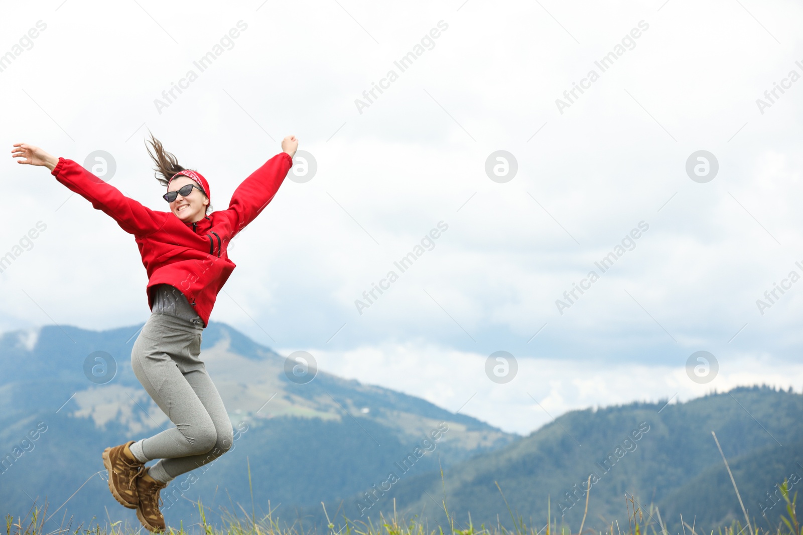 Photo of Happy young hiker jumping in mountains, low angle view. Space for text