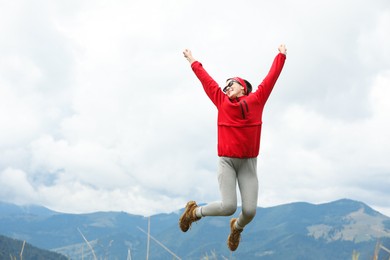 Photo of Happy young hiker jumping in mountains, low angle view. Space for text