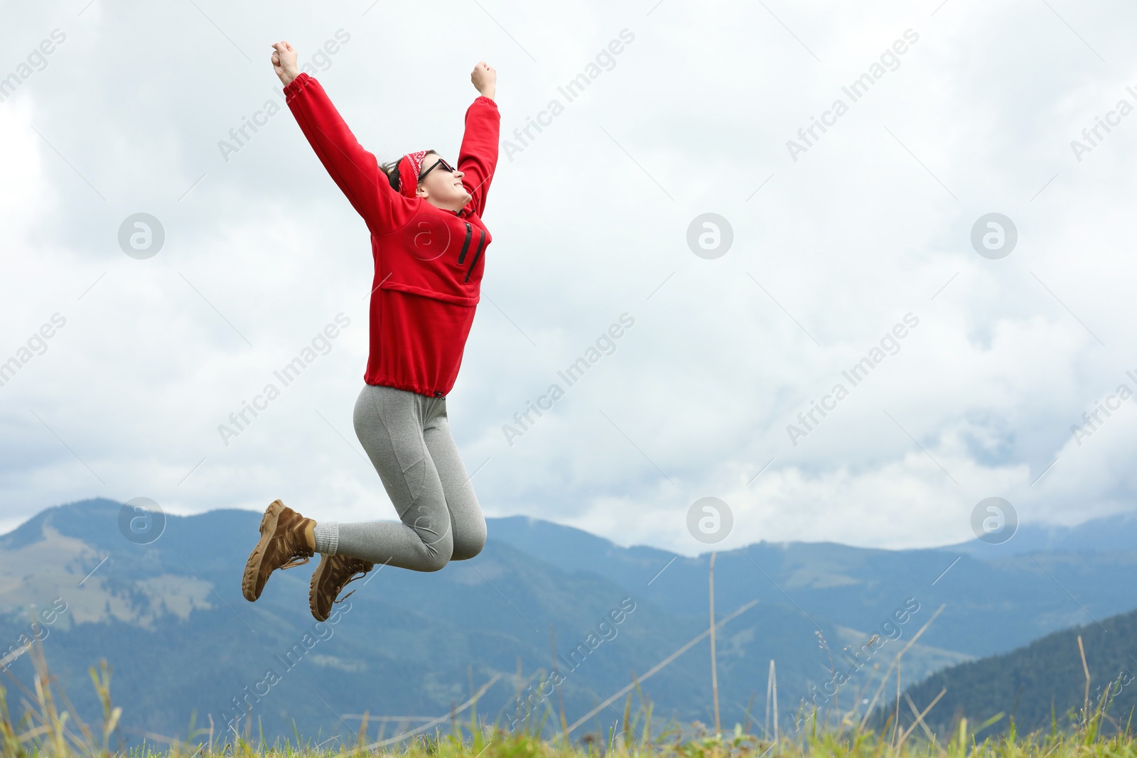 Photo of Happy young hiker jumping in mountains, low angle view. Space for text