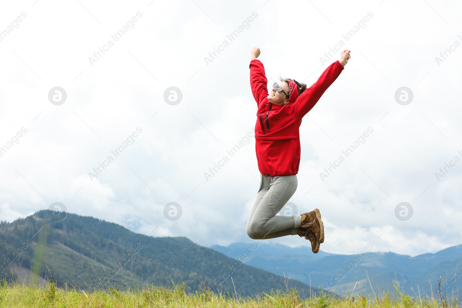 Photo of Happy young hiker jumping in mountains, low angle view. Space for text