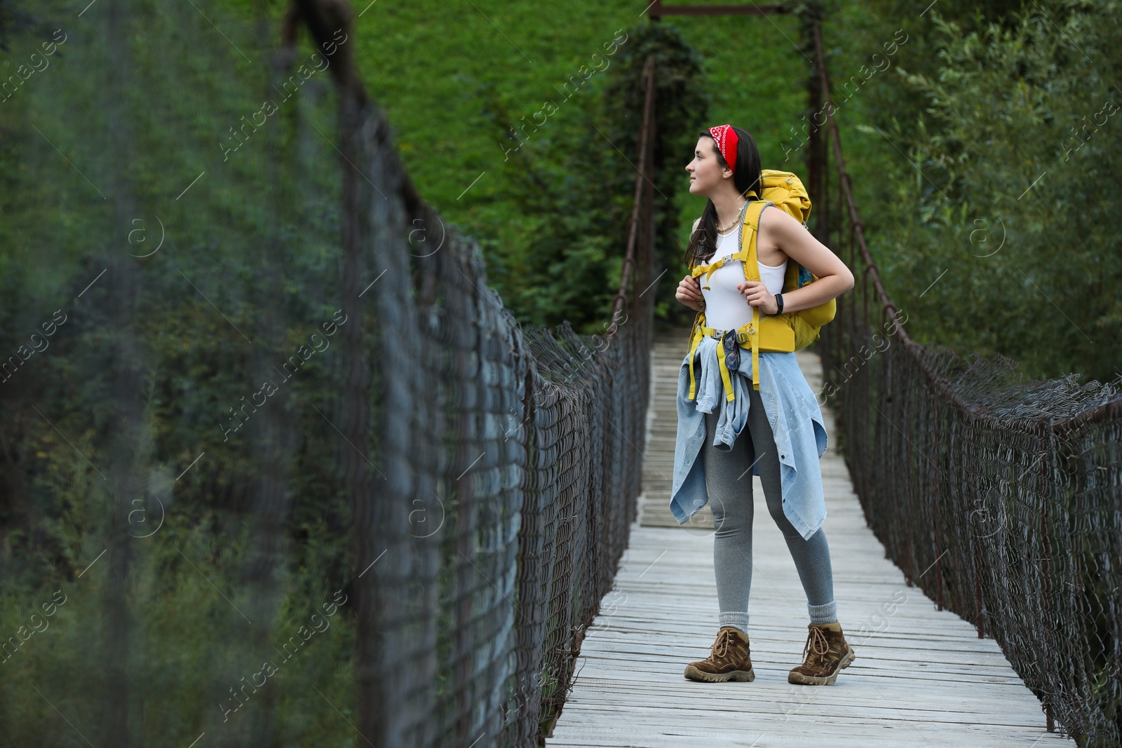 Photo of Young hiker walking on wooden bridge over river