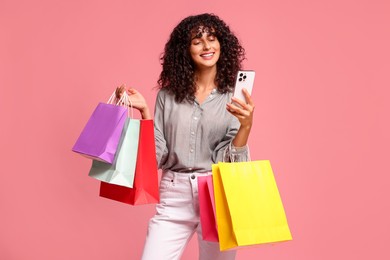 Photo of Smiling woman with colorful shopping bags and smartphone on pink background